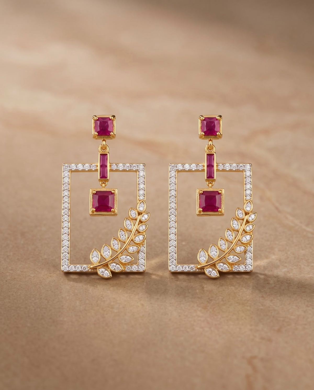 Close-up of gold geometric earrings with ruby and clear stone detailing